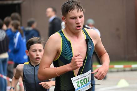 Zwei junge Athleten laufen beim Wettkampf, ein Junge in Badeanzug mit Nummer 105 und ein weiterer im Hintergrund.