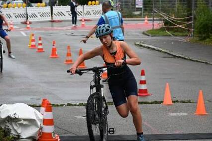 Junge Frau schiebt ihr Mountainbike zwischen Pylonen auf einem Wettkampfparcours.