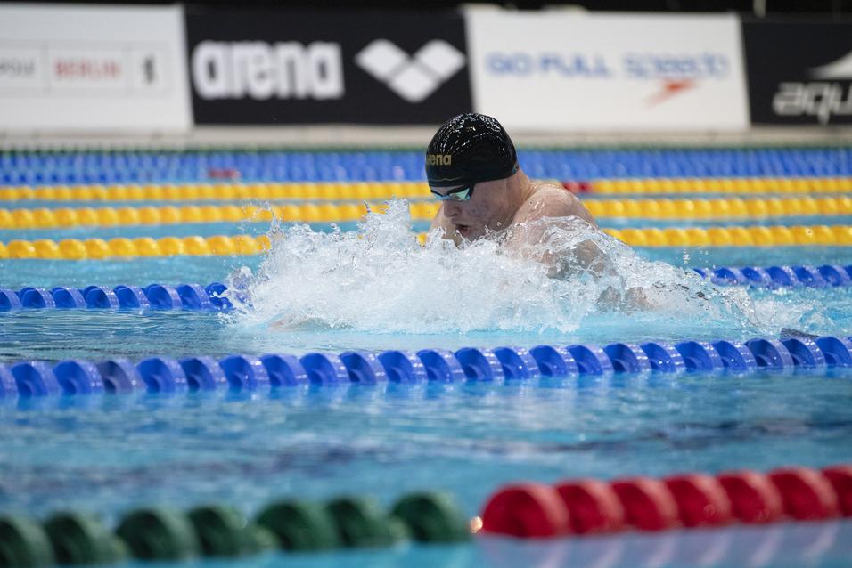 Schwimmer in einem Wettbewerb schwimmt mit Kraft im Bruststil durch das Wasser, Spritzwasser um ihn herum.