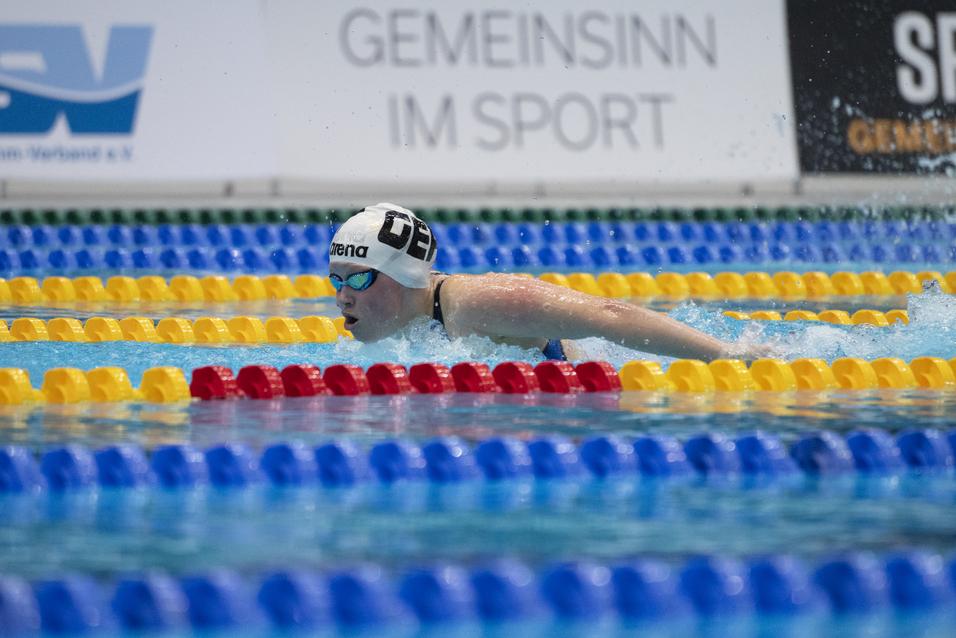 Schwimmerin im blauen Badeanzug vollzieht einen Wettkampf im Wasser, umgeben von bunten Schwimmbahnmarkierungen.