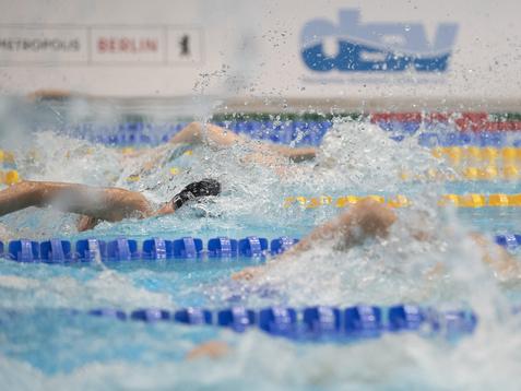 Wettkampf im Schwimmen mit mehreren Sportlern, die in einem Schwimmbecken mit spritzendem Wasser schwimmen.