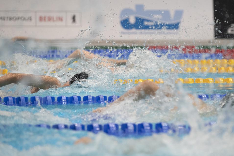 Wettkampf im Schwimmen mit mehreren Sportlern, die in einem Schwimmbecken mit spritzendem Wasser schwimmen.