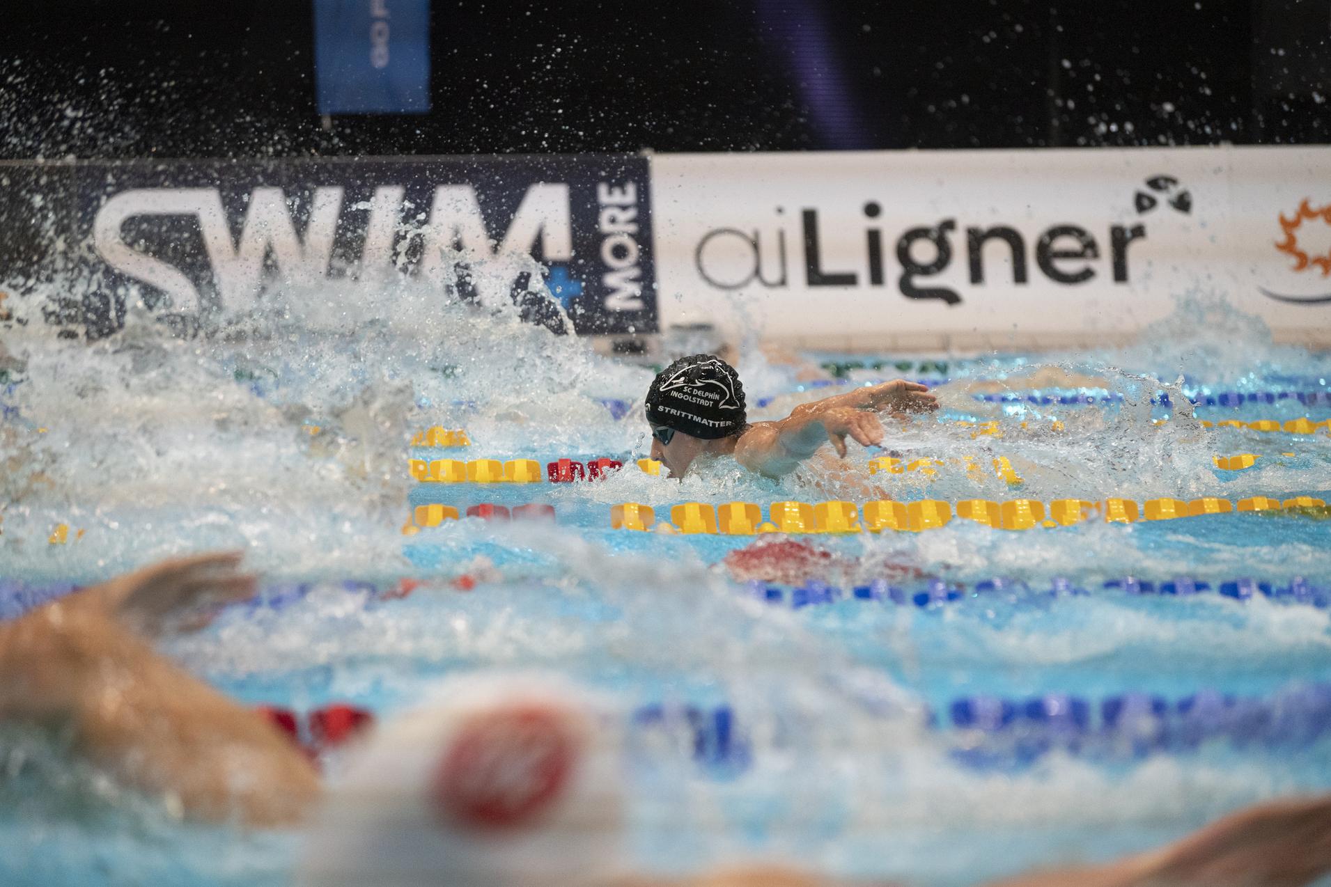 Schwimmer in einer Wettkampfsituation, Spritzer fliegen auf, w&auml;hrend er im Wasser schwimmt und die Bahn des Wettbewerbs nutzt.