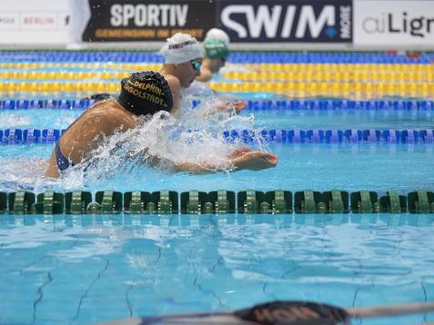Schwimmer in einem Wettkampf schwimmen im Wasser, w&auml;hrend Spritzer auf der Oberfl&auml;che entstehen.