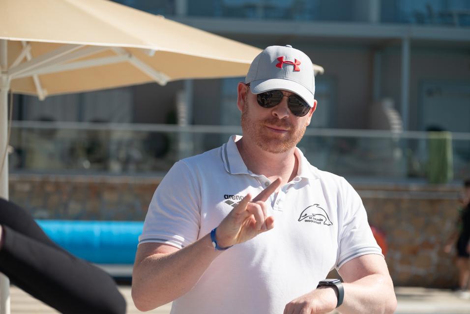 Mann mit Sonnenbrille und Baseballcap hält die Hand in einem Zeichen, während er im Freien steht.