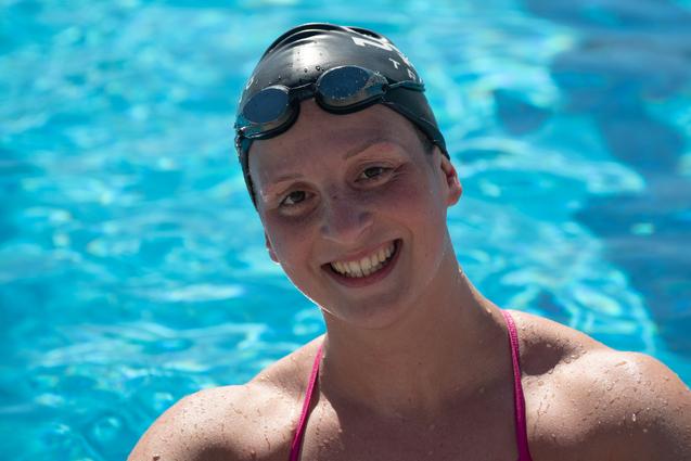 Lächelnde Schwimmerin in pinkem Badeanzug und Schwimmhaube posiert vor blauem Wasser eines Schwimmbeckens.